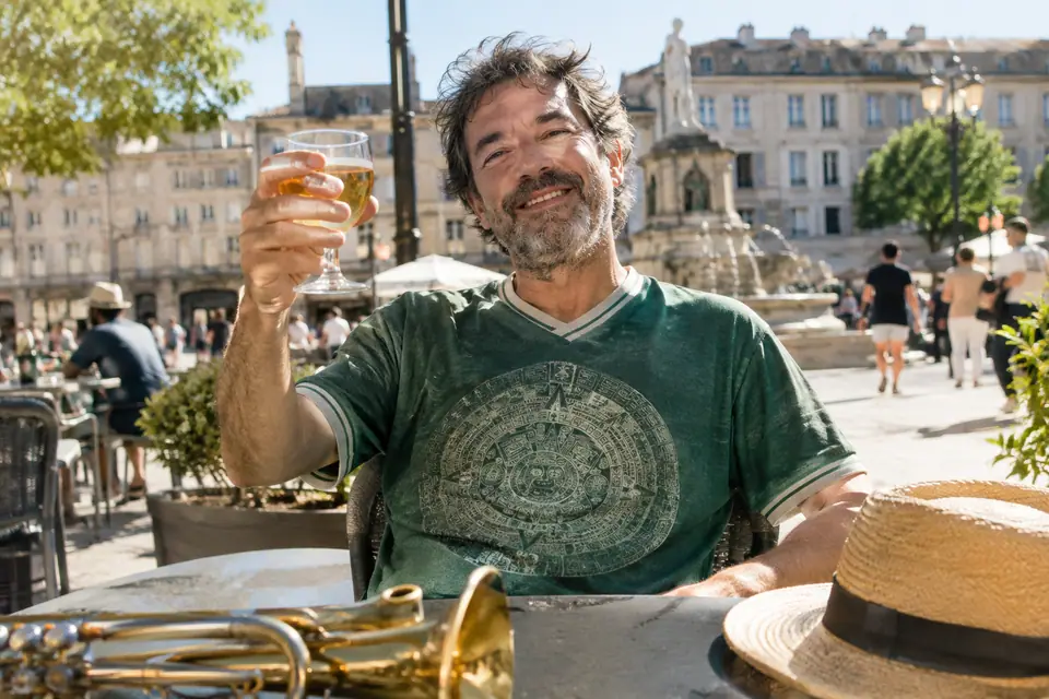Homme souriant en maillot de foot vert à grand motif circulaire sur une terrasse de café ensoleillée
