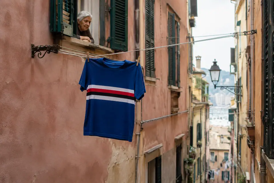 Maillot de foot bleu à bande blanche, rouge et noire séchant sur un fil à linge dans une ruelle