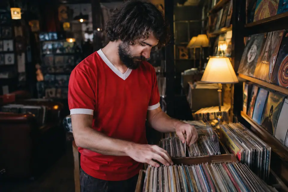 Homme barbu en maillot de foot rouge rétro feuilletant des vinyles dans une boutique d'occasion